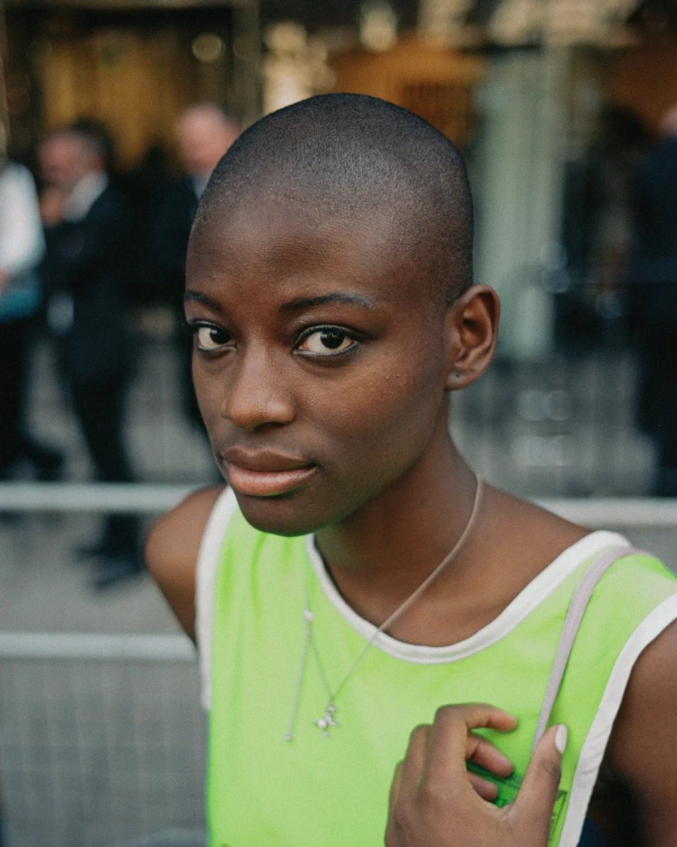 A young woman in a green vest looks straight at the camera outside London Fashion Week.